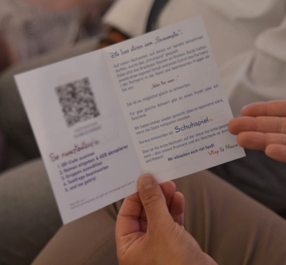 Gast hält die Einladungskarte zum Schuhspiel mit QR-Code und den fünf Schritten zum Beitritt in den Händen.