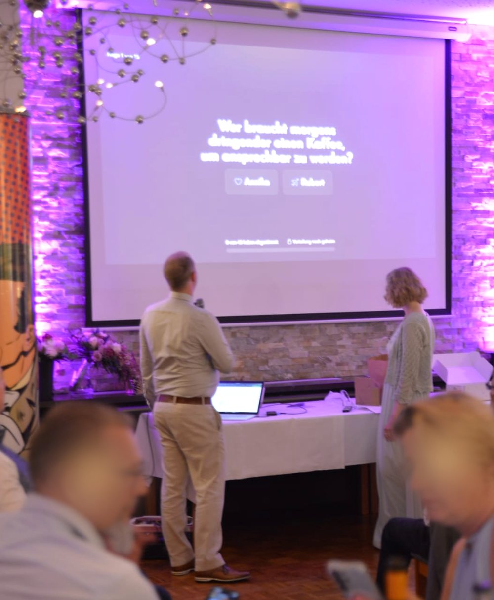 Blick in den Saal: Auf der Leinwand steht die Schuhspiel-Frage, im Vordergrund verfolgen Gäste die Runde am Smartphone.